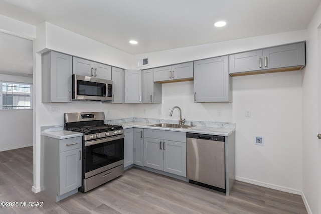 kitchen featuring appliances with stainless steel finishes, gray cabinets, light countertops, and a sink