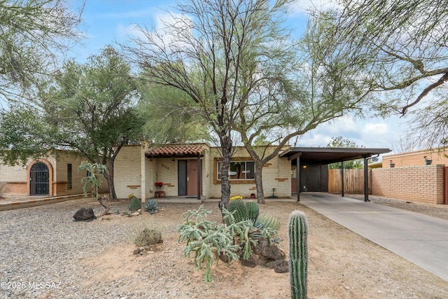 view of front of property featuring brick siding, a tile roof, fence, concrete driveway, and a carport