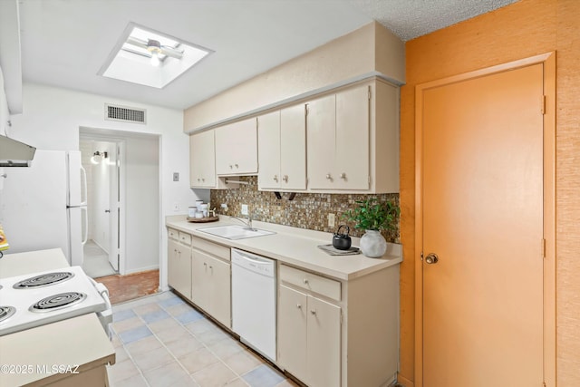 kitchen with white appliances, a skylight, visible vents, light countertops, and a sink