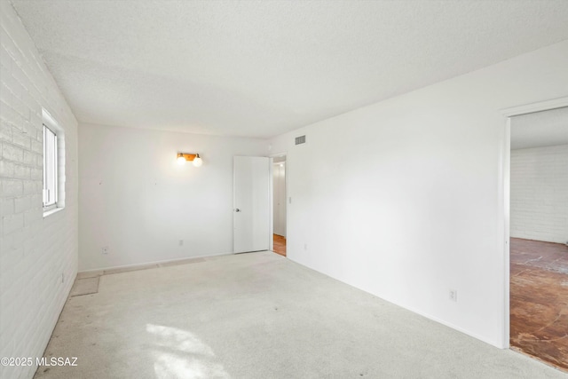 carpeted empty room with visible vents, a textured ceiling, and brick wall