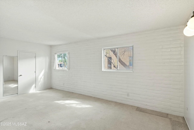 carpeted spare room featuring a textured ceiling and brick wall