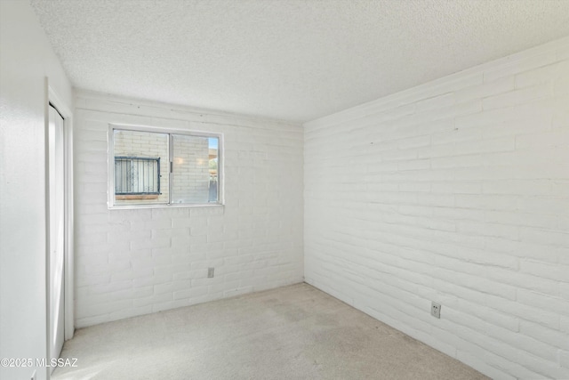 carpeted spare room with a textured ceiling and brick wall