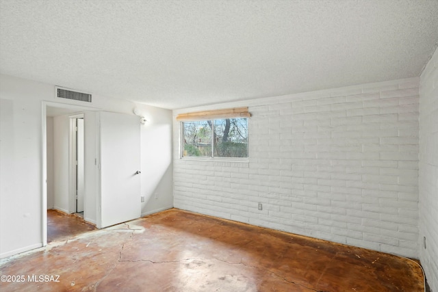 unfurnished room with brick wall, visible vents, and a textured ceiling