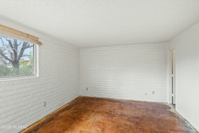 empty room with concrete floors, a textured ceiling, and brick wall