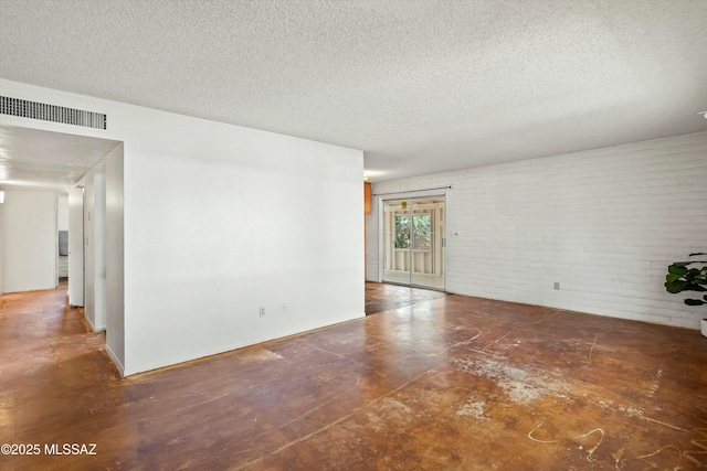 empty room featuring a textured ceiling, brick wall, visible vents, and concrete flooring