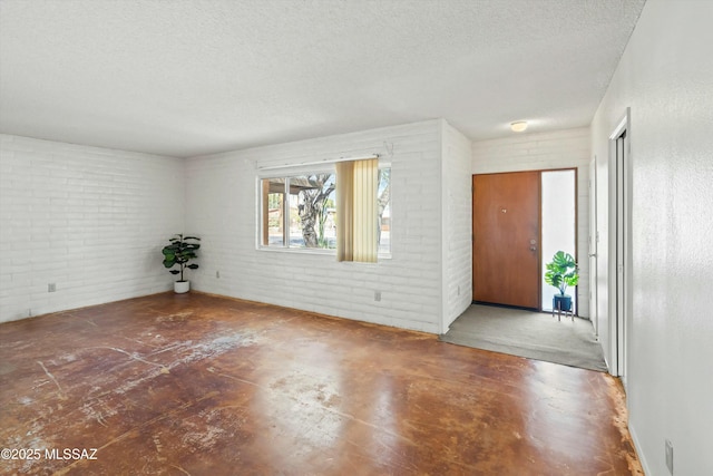 unfurnished room featuring concrete flooring, a textured ceiling, and brick wall