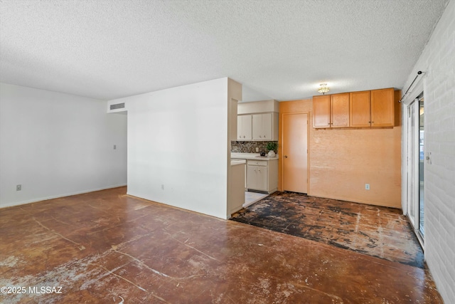 interior space with a textured ceiling, concrete flooring, visible vents, and decorative backsplash