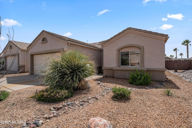 view of front of house featuring a tile roof, stucco siding, fence, driveway, and a garage