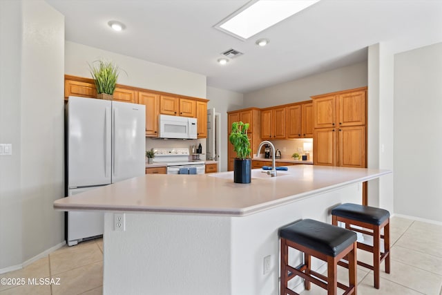 kitchen with light countertops, white appliances, a kitchen bar, an island with sink, and light tile patterned floors