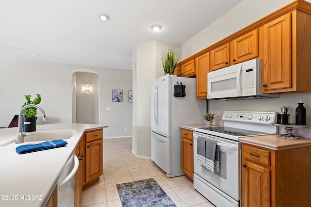 kitchen featuring white appliances, light tile patterned floors, a sink, arched walkways, and brown cabinets
