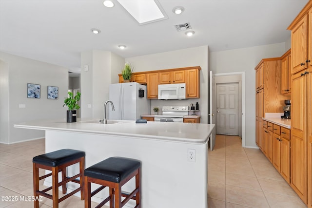 kitchen with white appliances, light tile patterned floors, a sink, a skylight, and visible vents