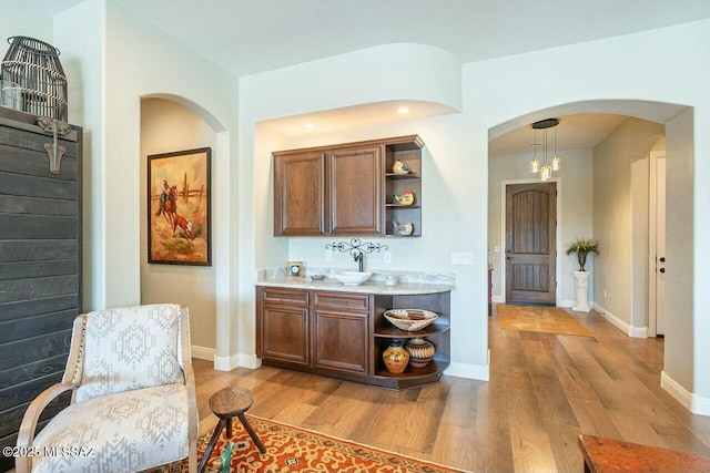 bar featuring arched walkways, light wood-style flooring, and baseboards