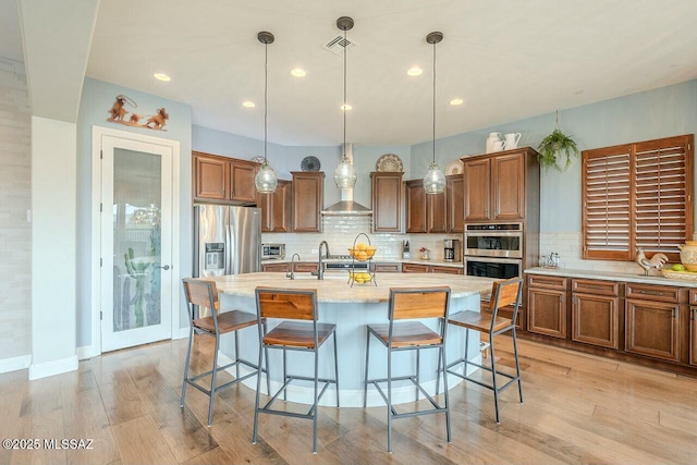 kitchen featuring visible vents, a breakfast bar area, brown cabinets, stainless steel appliances, and light wood-style floors