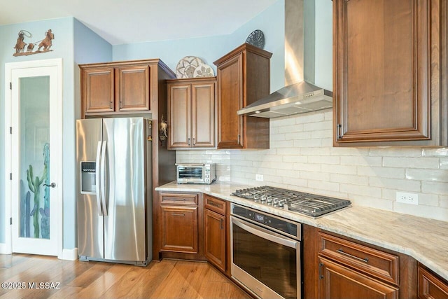 kitchen featuring a toaster, decorative backsplash, appliances with stainless steel finishes, light wood-style floors, and wall chimney range hood