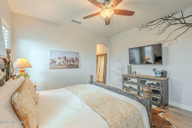 bedroom featuring baseboards, visible vents, a ceiling fan, arched walkways, and wood finished floors