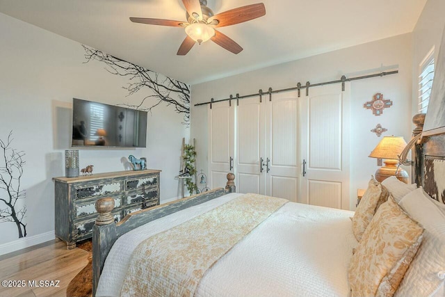 bedroom featuring a ceiling fan, a barn door, baseboards, and wood finished floors