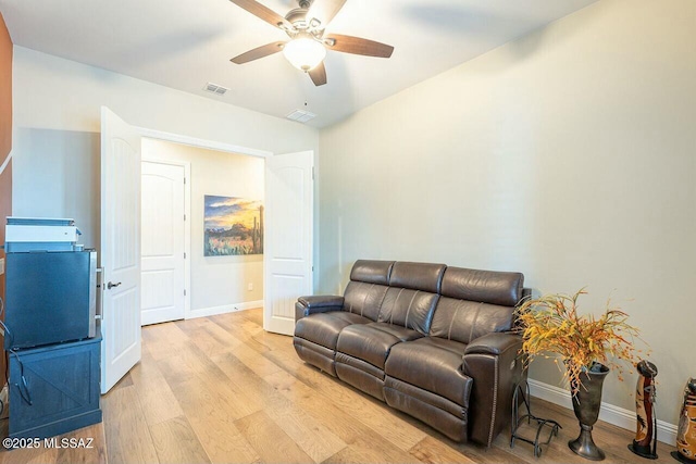 living area featuring baseboards, light wood-style flooring, visible vents, and a ceiling fan