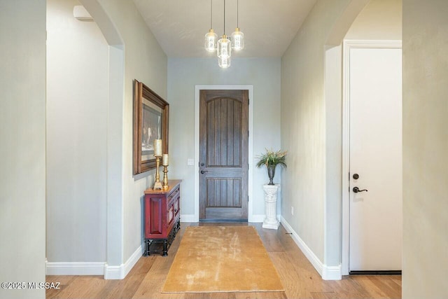 entrance foyer featuring light wood finished floors, baseboards, and arched walkways