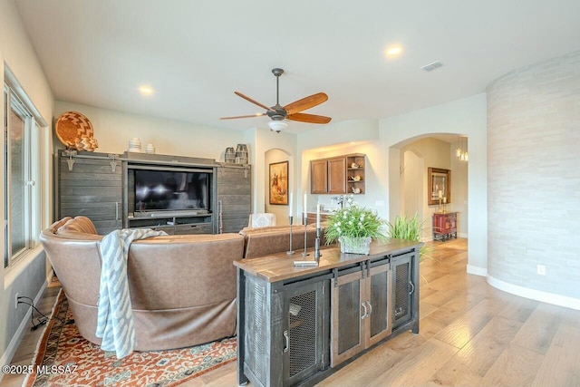 living area featuring light wood finished floors, visible vents, arched walkways, baseboards, and ceiling fan