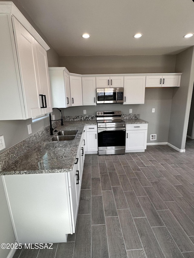 kitchen with stainless steel appliances, wood finish floors, a sink, white cabinets, and dark stone counters