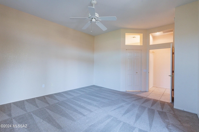 carpeted empty room with tile patterned floors and a ceiling fan