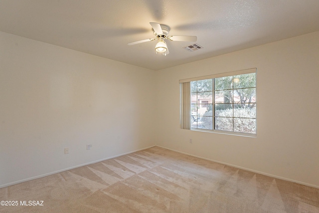 empty room featuring visible vents, light colored carpet, baseboards, and a ceiling fan