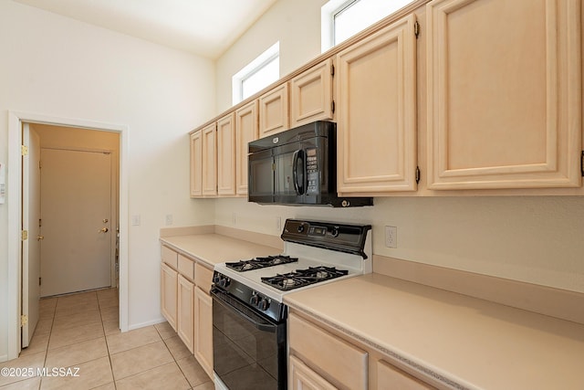 kitchen featuring black microwave, light brown cabinetry, light countertops, light tile patterned floors, and gas stove