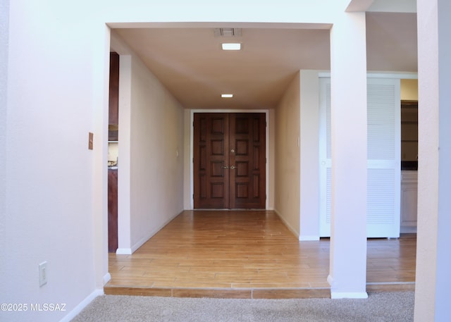 hall featuring visible vents, baseboards, and wood finished floors