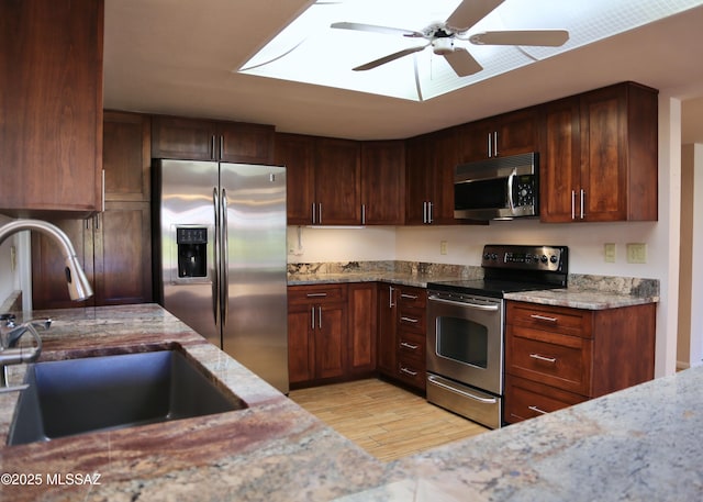 kitchen with light stone counters, a skylight, a sink, ceiling fan, and stainless steel appliances