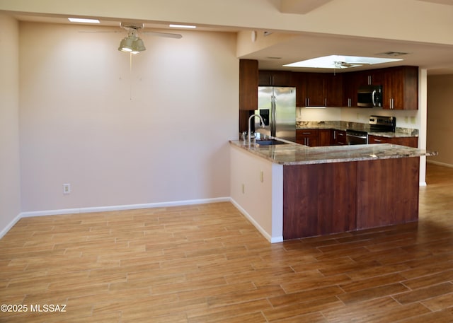 kitchen featuring a ceiling fan, a peninsula, light wood-style flooring, a sink, and stainless steel appliances