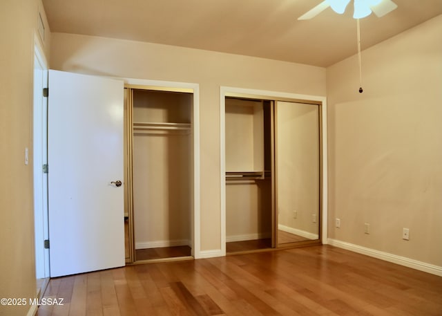 unfurnished bedroom featuring baseboards, multiple closets, wood finished floors, and a ceiling fan