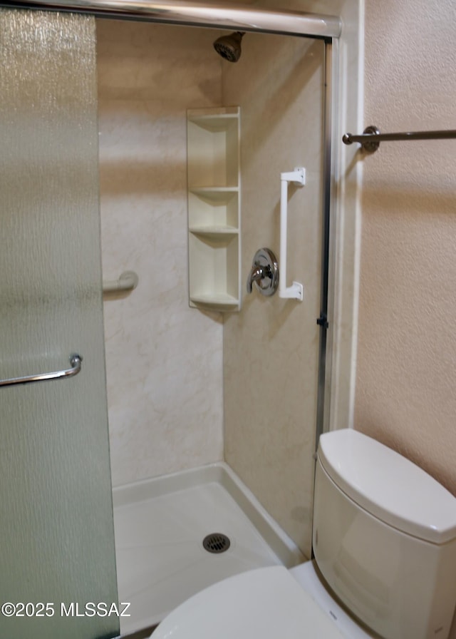 bathroom with a shower stall, toilet, and a textured wall