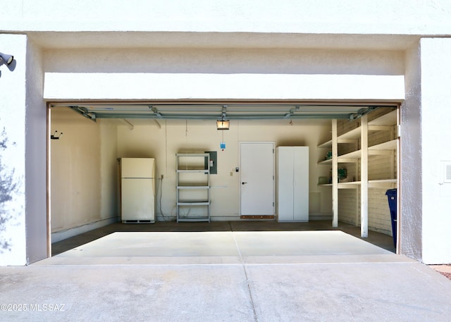 garage with electric panel, driveway, freestanding refrigerator, and a garage door opener