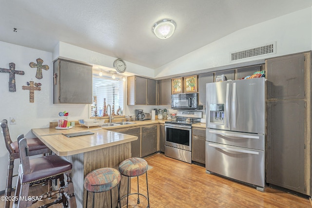 kitchen with stainless steel appliances, lofted ceiling, visible vents, a sink, and a peninsula