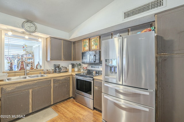 kitchen with visible vents, appliances with stainless steel finishes, vaulted ceiling, a sink, and light wood-type flooring