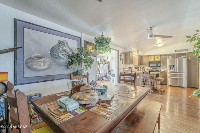 dining area with light wood finished floors, visible vents, vaulted ceiling, and a textured ceiling