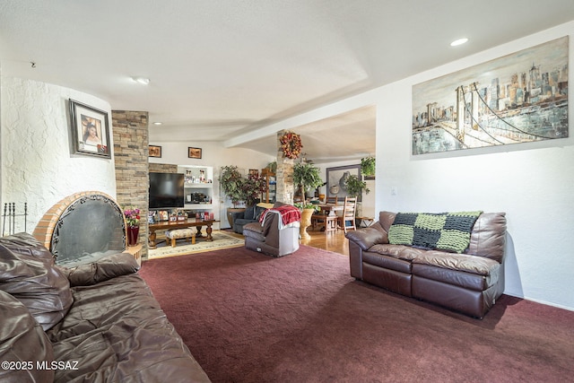 carpeted living room featuring vaulted ceiling with beams, a fireplace, and a textured wall