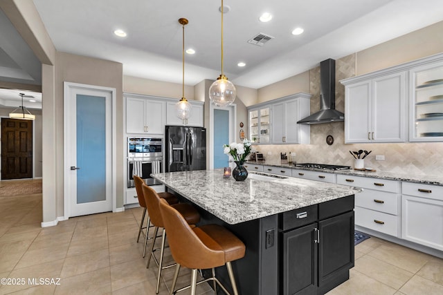 kitchen with stainless steel appliances, a kitchen island, visible vents, decorative backsplash, and wall chimney exhaust hood