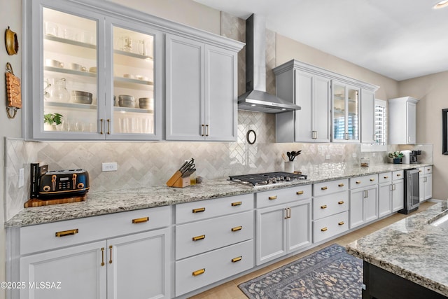 kitchen with light stone countertops, wall chimney exhaust hood, stainless steel gas cooktop, and tasteful backsplash