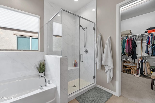 full bathroom featuring a spacious closet, a shower stall, a bath, and baseboards