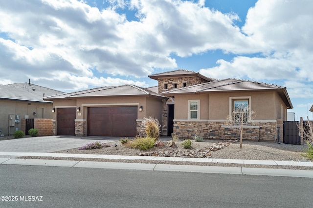 prairie-style house with stone siding, an attached garage, fence, and stucco siding