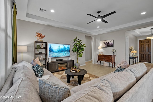 living room featuring recessed lighting, visible vents, a tray ceiling, and a glass covered fireplace