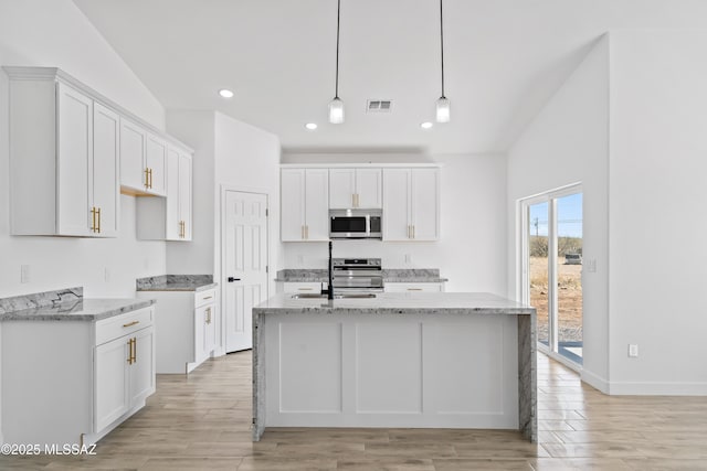 kitchen featuring visible vents, white cabinets, appliances with stainless steel finishes, light stone countertops, and a center island with sink