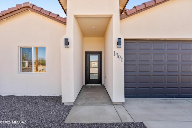 view of exterior entry with a tiled roof, an attached garage, driveway, and stucco siding