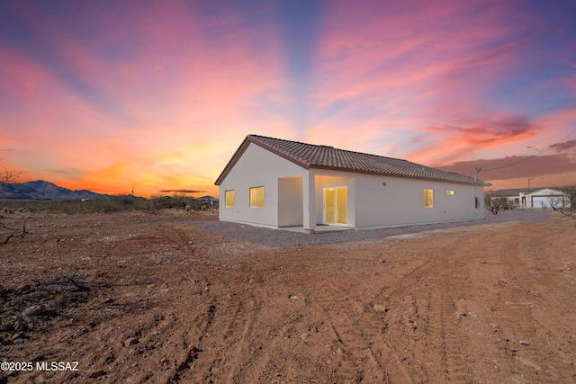 back of house at dusk with a tile roof and stucco siding