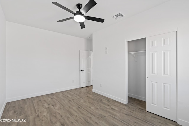 unfurnished bedroom with wood finished floors, a ceiling fan, visible vents, baseboards, and a closet