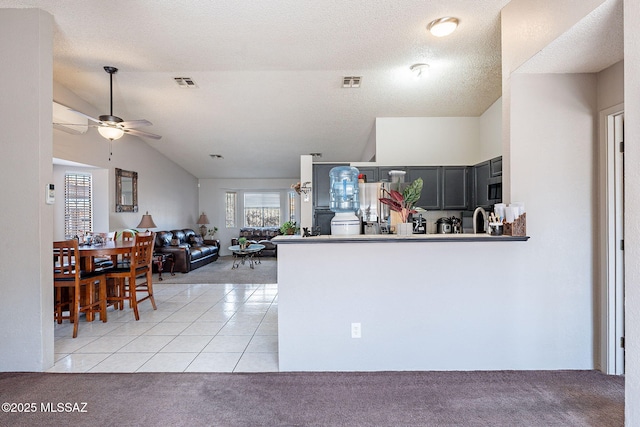 kitchen with light tile patterned flooring, light colored carpet, visible vents, vaulted ceiling, and appliances with stainless steel finishes