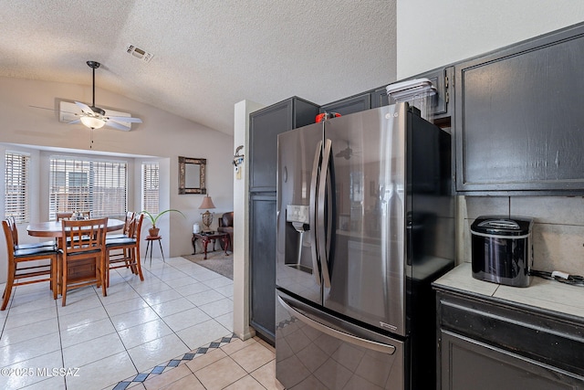 kitchen with light tile patterned floors, visible vents, a ceiling fan, vaulted ceiling, and stainless steel fridge