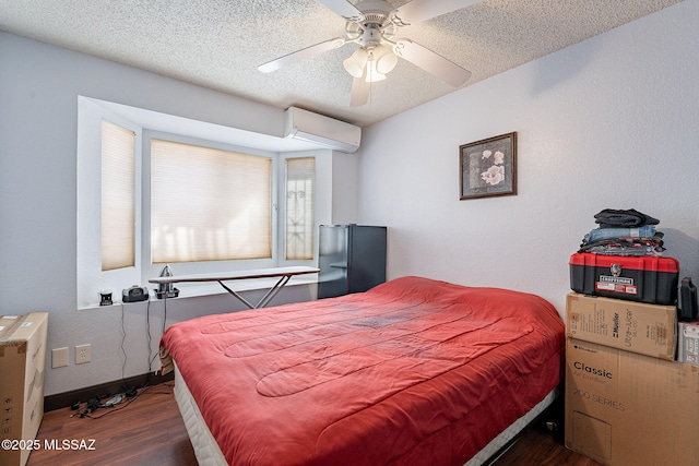 bedroom with a textured ceiling, a wall unit AC, wood finished floors, baseboards, and freestanding refrigerator