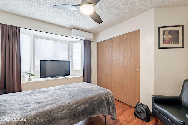 bedroom with a closet, multiple windows, an AC wall unit, and wood finished floors